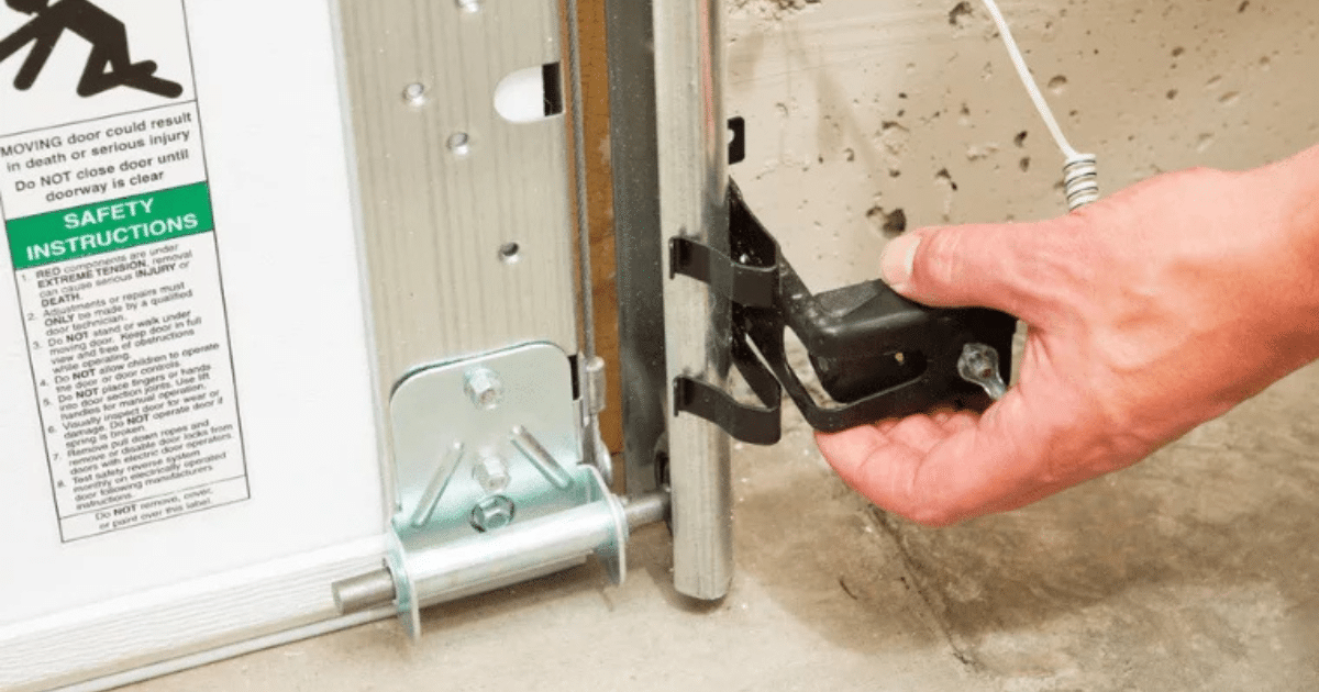Hand aligning garage door safety sensor.