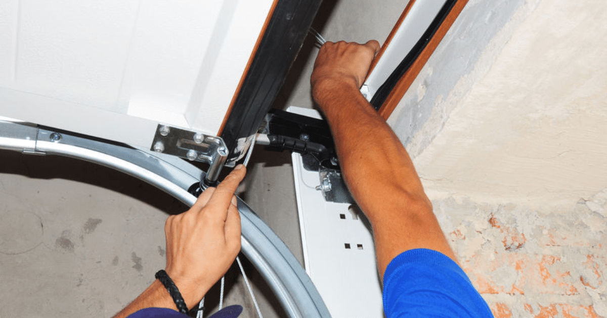 Hands adjusting garage door cable track.