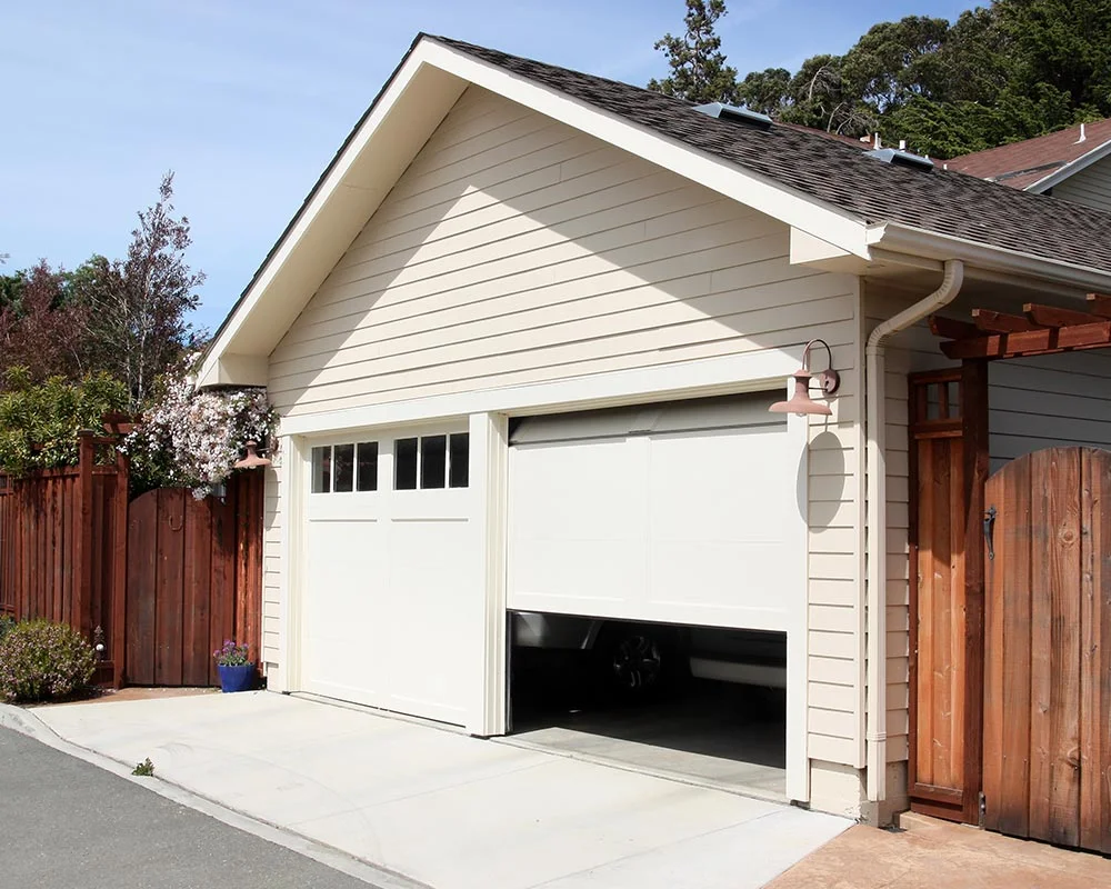 A residential garage with a white, modern sectional door opening automatically on a paved driveway to reveal an Installed Garage Door.
